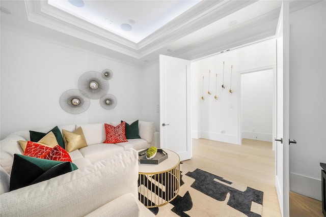 living room with ornamental molding, light wood-type flooring, and a raised ceiling