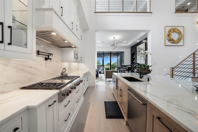 kitchen with light wood-type flooring, stainless steel appliances, light stone countertops, sink, and white cabinets