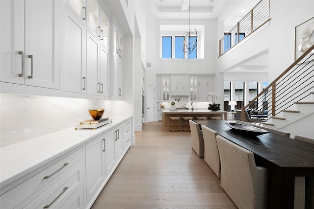 kitchen with light wood-type flooring, white cabinetry, hanging light fixtures, light stone countertops, and decorative backsplash