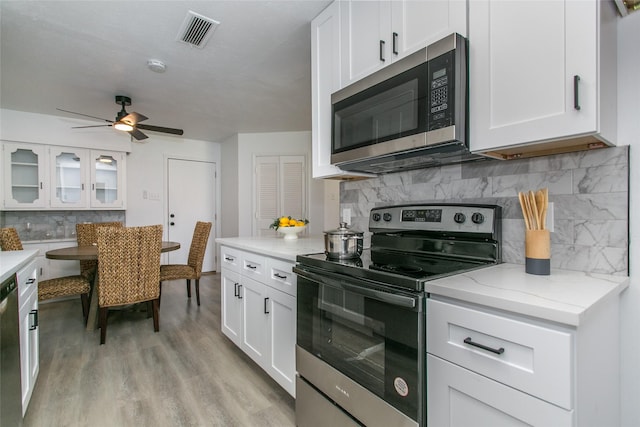 kitchen featuring appliances with stainless steel finishes, white cabinetry, decorative backsplash, light stone countertops, and light hardwood / wood-style flooring