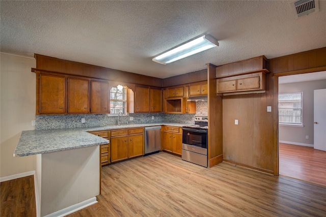 kitchen with decorative backsplash, kitchen peninsula, stainless steel appliances, plenty of natural light, and light wood-type flooring