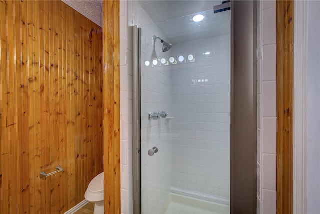 bathroom featuring toilet, a shower with shower door, and wood walls