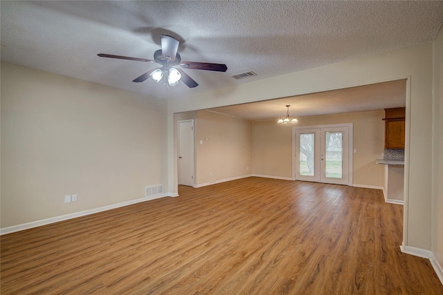 unfurnished living room featuring ceiling fan with notable chandelier, a textured ceiling, light hardwood / wood-style floors, and french doors