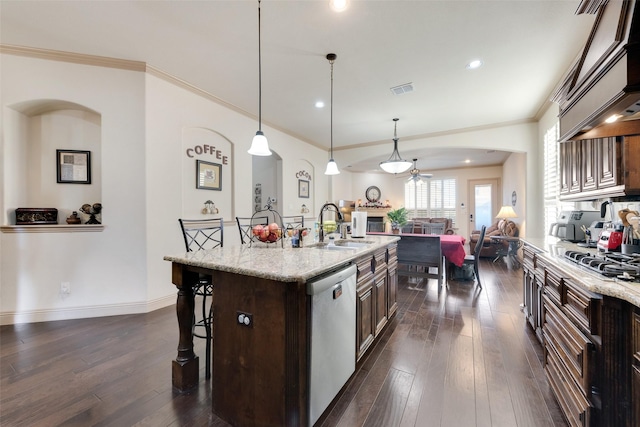 kitchen with appliances with stainless steel finishes, hanging light fixtures, a kitchen breakfast bar, dark brown cabinetry, and a center island with sink