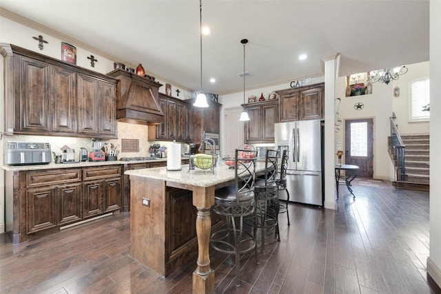 kitchen with pendant lighting, appliances with stainless steel finishes, dark brown cabinets, tasteful backsplash, and a center island with sink