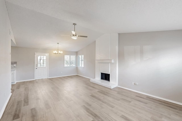 unfurnished living room featuring a brick fireplace, ceiling fan with notable chandelier, vaulted ceiling, and light hardwood / wood-style floors