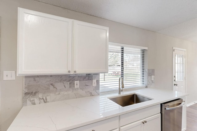 kitchen featuring white cabinetry, sink, stainless steel dishwasher, and light stone counters