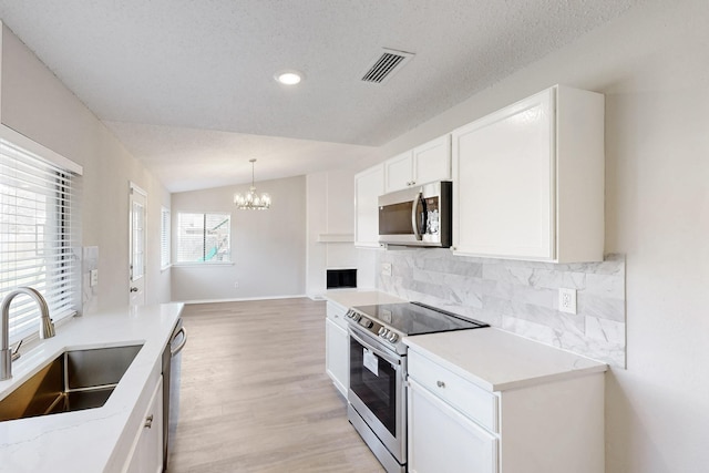 kitchen featuring vaulted ceiling, appliances with stainless steel finishes, white cabinetry, sink, and decorative backsplash