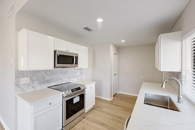 kitchen with sink, light wood-type flooring, white cabinets, and appliances with stainless steel finishes