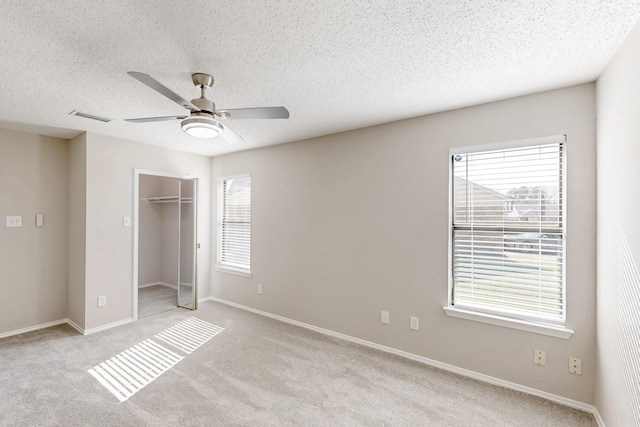 unfurnished bedroom with a textured ceiling, light colored carpet, a closet, and ceiling fan