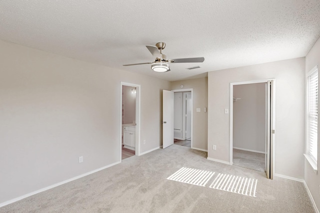 unfurnished bedroom with light colored carpet, a closet, a textured ceiling, and ensuite bathroom