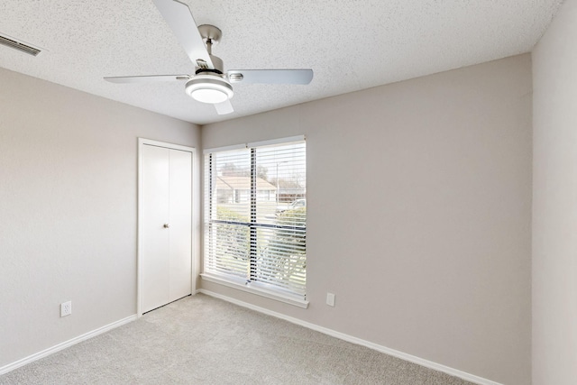 empty room with ceiling fan, light carpet, and a textured ceiling