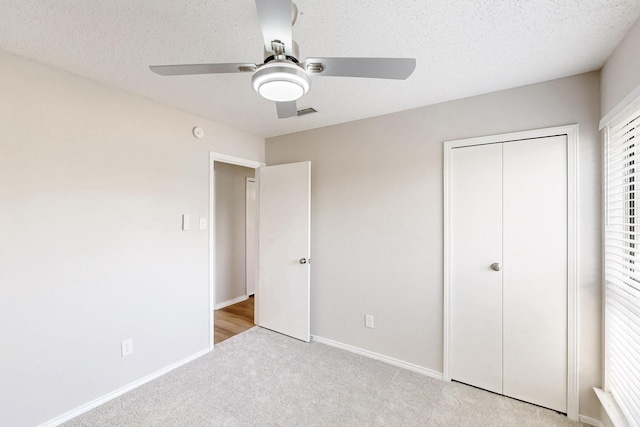 unfurnished bedroom with light carpet, ceiling fan, a closet, and a textured ceiling