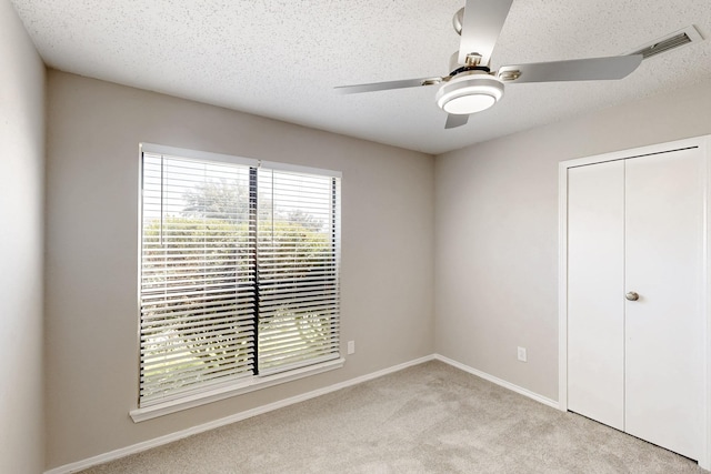 unfurnished bedroom featuring ceiling fan, light carpet, a textured ceiling, and a closet