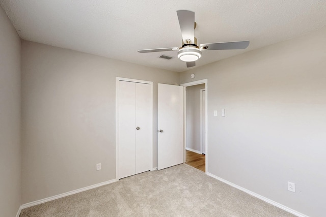 unfurnished bedroom featuring light carpet, ceiling fan, a closet, and a textured ceiling