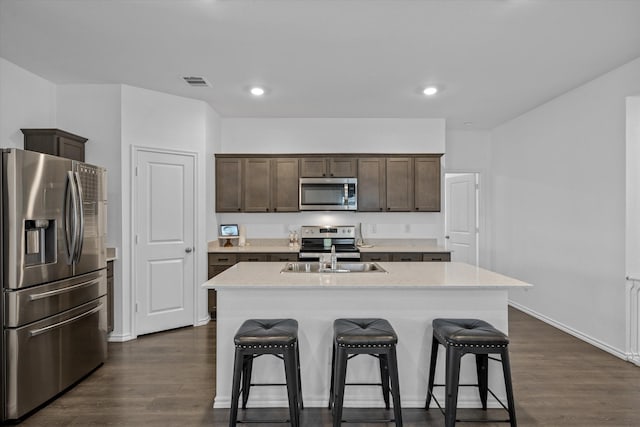 kitchen with dark wood-type flooring, dark brown cabinetry, sink, appliances with stainless steel finishes, and a kitchen island with sink