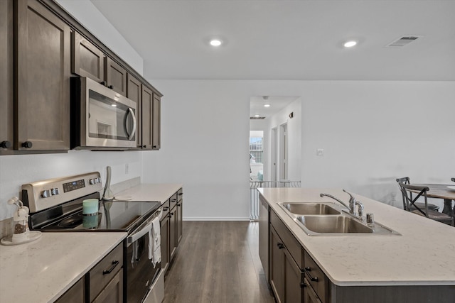 kitchen featuring sink, dark brown cabinets, appliances with stainless steel finishes, dark hardwood / wood-style floors, and a kitchen island with sink