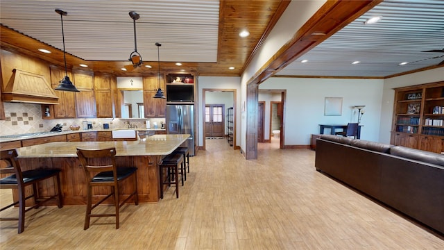 kitchen featuring stainless steel appliances, light stone countertops, custom range hood, a kitchen bar, and decorative light fixtures