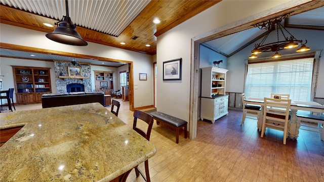 dining area featuring lofted ceiling, wood-type flooring, wooden ceiling, ornamental molding, and a fireplace