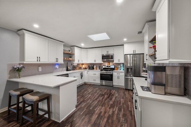 kitchen featuring white cabinetry, appliances with stainless steel finishes, a kitchen bar, and kitchen peninsula