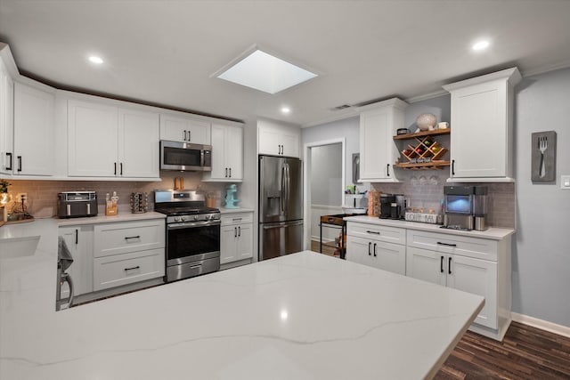 kitchen with a skylight, stainless steel appliances, light stone countertops, white cabinets, and dark hardwood / wood-style flooring