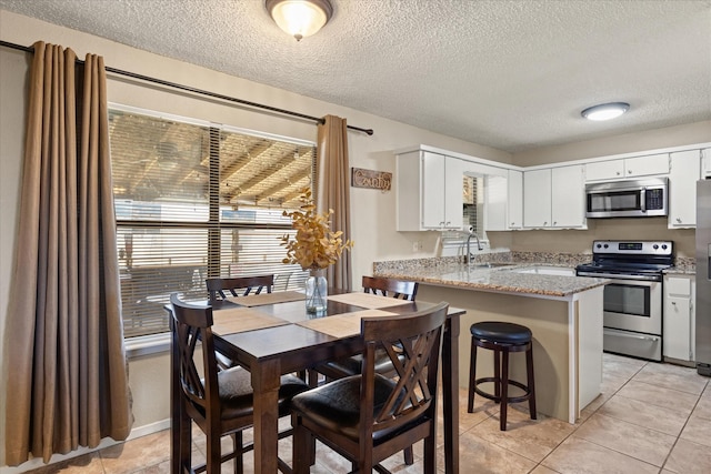 kitchen featuring appliances with stainless steel finishes, light stone countertops, white cabinets, light tile patterned flooring, and kitchen peninsula