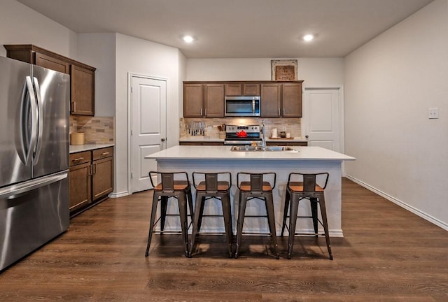 kitchen featuring dark wood-type flooring, appliances with stainless steel finishes, sink, and an island with sink