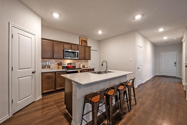 kitchen with appliances with stainless steel finishes, sink, a kitchen island with sink, and dark hardwood / wood-style floors