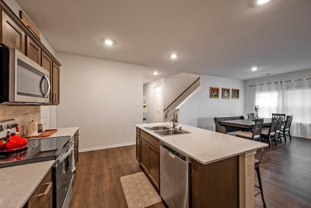 kitchen with appliances with stainless steel finishes, dark hardwood / wood-style floors, sink, backsplash, and a kitchen island with sink