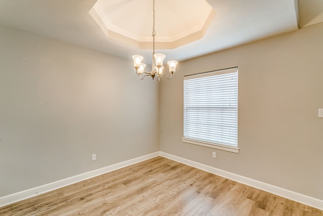 unfurnished room featuring wood-type flooring, ornamental molding, an inviting chandelier, and a tray ceiling