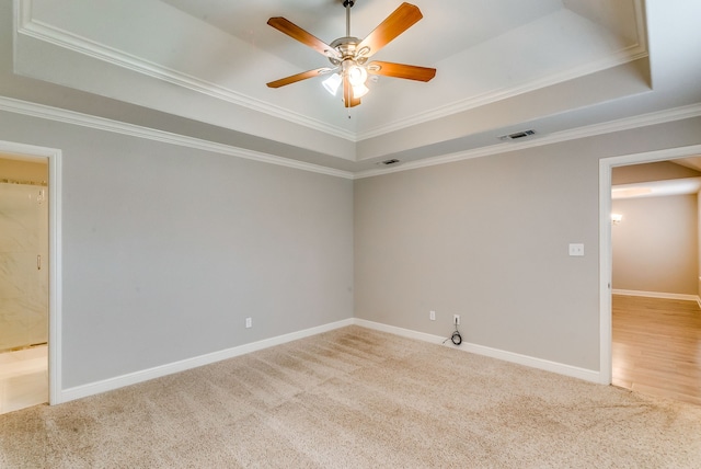 carpeted spare room with a raised ceiling, ornamental molding, and ceiling fan