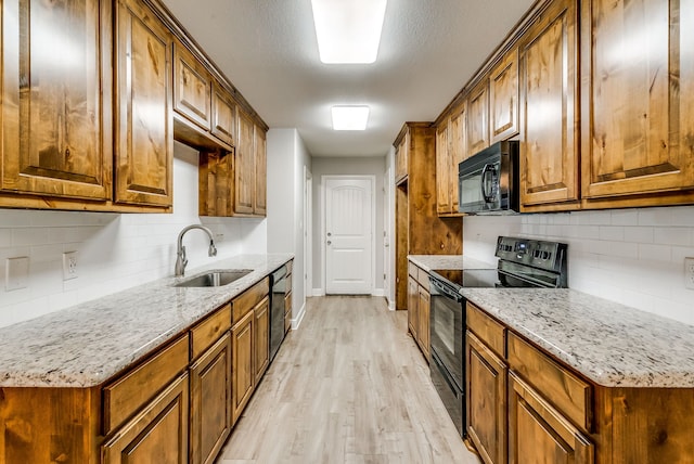 kitchen with sink, light stone counters, black appliances, decorative backsplash, and light wood-type flooring