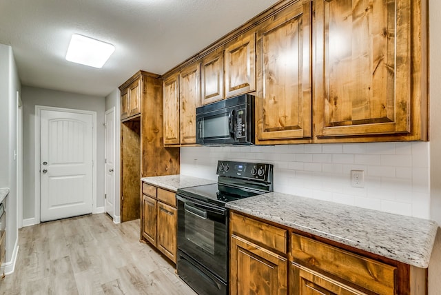 kitchen featuring light stone counters, decorative backsplash, black appliances, and light hardwood / wood-style floors