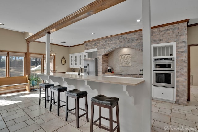 9808 Neesonwood Dr, Shreveport, LA 71106 - kitchen featuring appliances with stainless steel finishes, light countertops, white cabinets, a kitchen breakfast bar, and ornamental molding