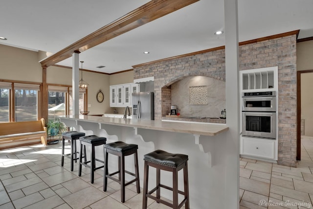 kitchen with glass insert cabinets, a kitchen breakfast bar, stainless steel appliances, light countertops, and white cabinetry