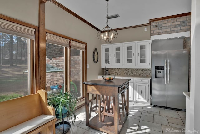 9808 Neesonwood Dr, Shreveport, LA 71106 - kitchen with stainless steel fridge, a chandelier, white cabinets, light tile patterned floors, and glass insert cabinets