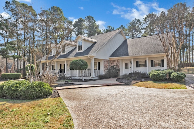 new england style home with a porch, roof with shingles, and driveway