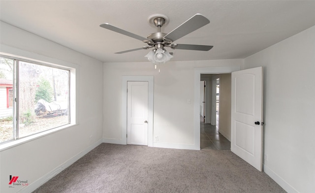 unfurnished bedroom with multiple windows, dark carpet, and ceiling fan