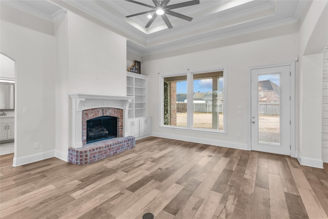 unfurnished living room with ornamental molding, a raised ceiling, light hardwood / wood-style floors, and a brick fireplace