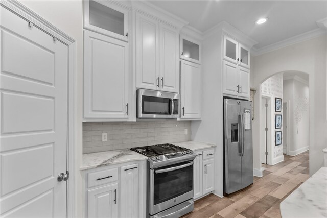 kitchen with white cabinetry, appliances with stainless steel finishes, ornamental molding, and backsplash