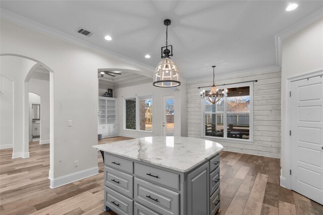 kitchen with light stone counters, hanging light fixtures, ornamental molding, and a center island