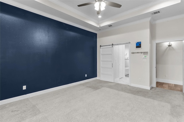 empty room featuring light colored carpet, ceiling fan, a raised ceiling, crown molding, and a barn door