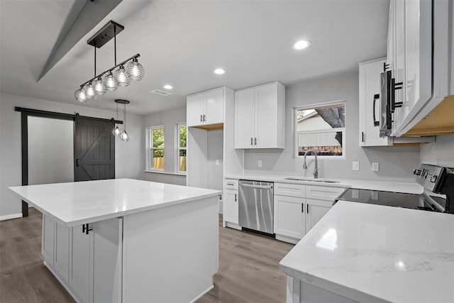 kitchen featuring appliances with stainless steel finishes, decorative light fixtures, sink, white cabinets, and a barn door