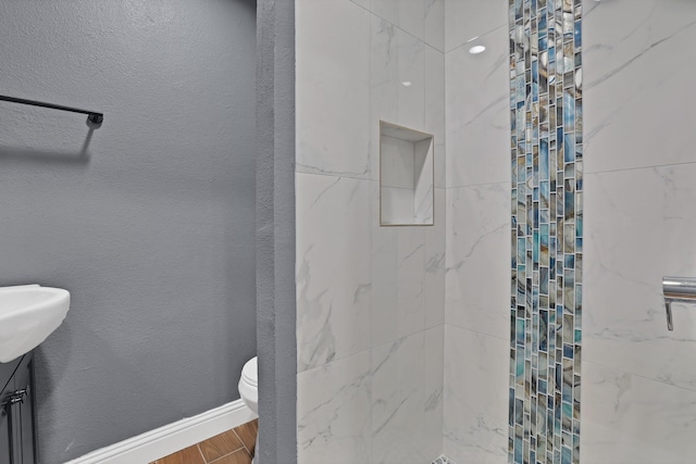 bathroom with toilet, hardwood / wood-style floors, and a tile shower