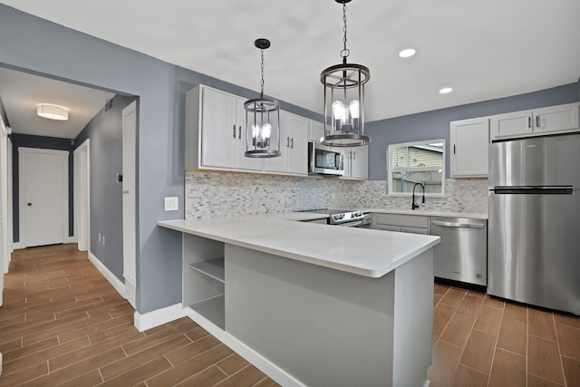 kitchen featuring hanging light fixtures, stainless steel appliances, white cabinets, decorative backsplash, and kitchen peninsula