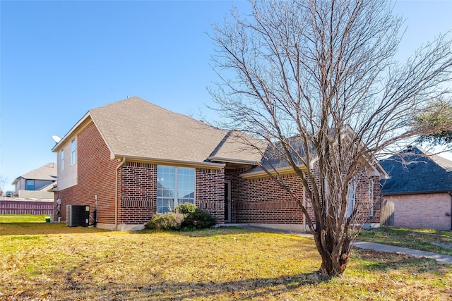 view of front facade with brick siding, a front lawn, a shingled roof, and cooling unit