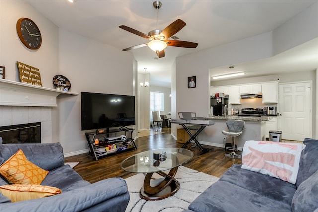 living room with dark wood-style floors, a tile fireplace, baseboards, and a ceiling fan