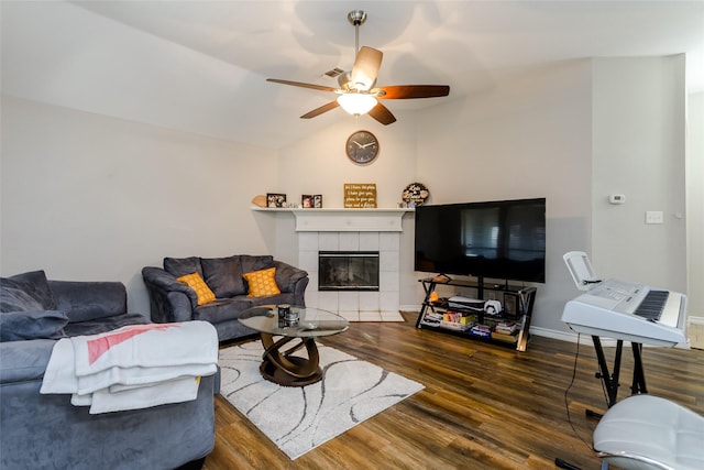 living room with baseboards, dark wood finished floors, a tiled fireplace, lofted ceiling, and ceiling fan