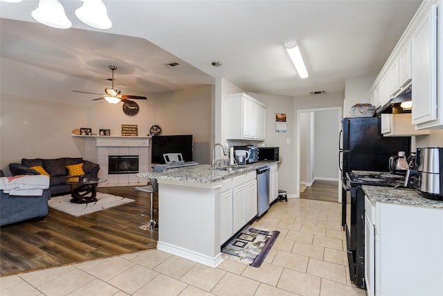 kitchen with a fireplace, a kitchen breakfast bar, open floor plan, white cabinets, and black appliances