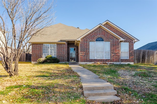 ranch-style house with a shingled roof, brick siding, fence, and a front lawn